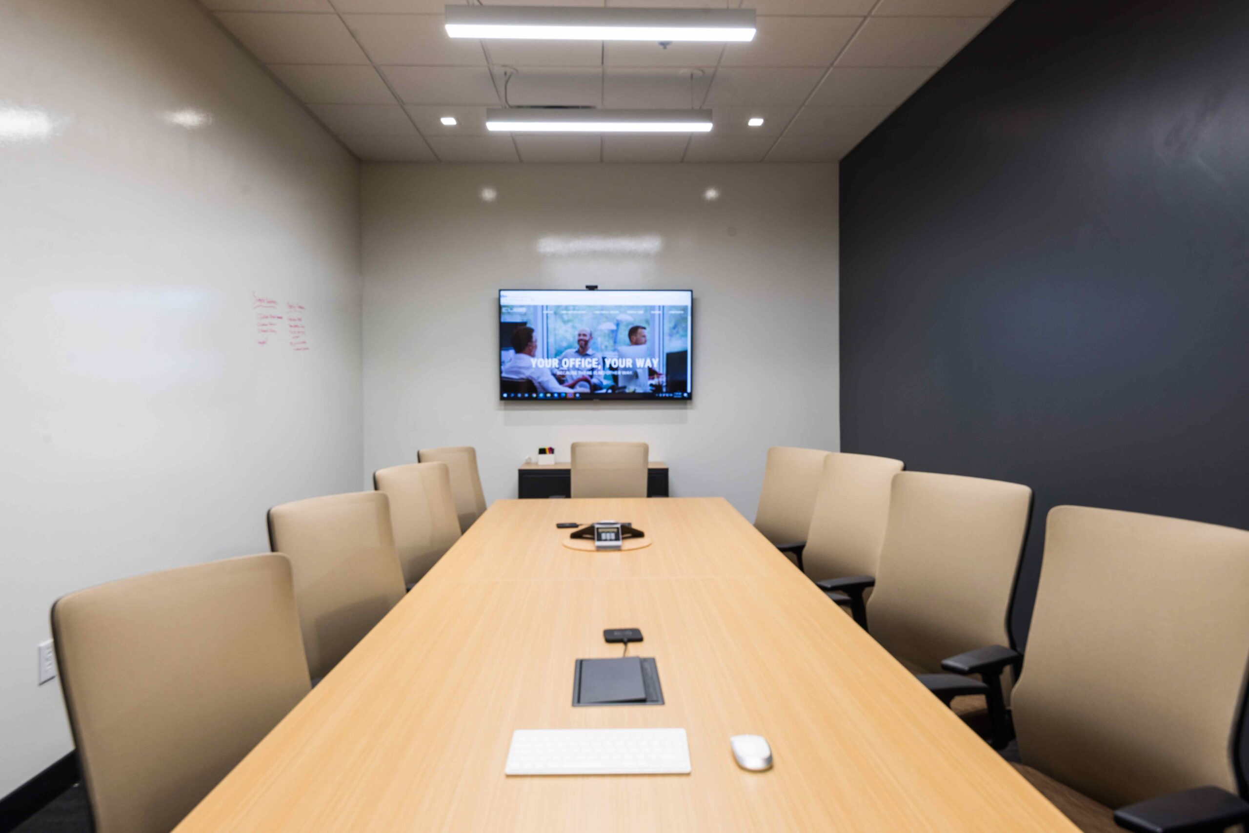 Dallas Meeting Space. Conference room table shares space for 9 people, space includes a TV and whiteboard.
